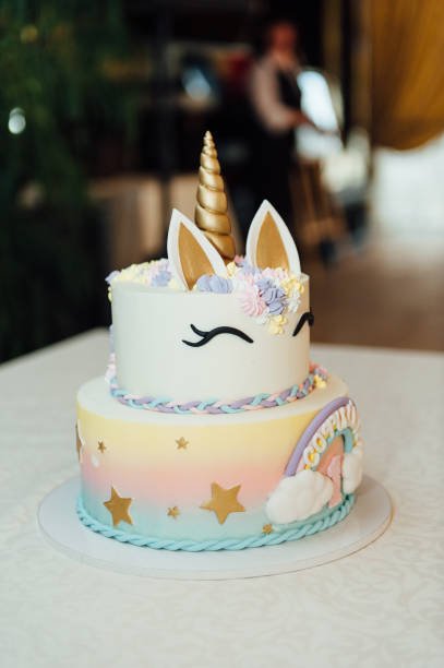 Kids birthday party decoration and cake. Decorated table for child birthday celebration. Rainbow unicorn cake for little girl. Room with festive balloons, colorful banners in baby pastel color.