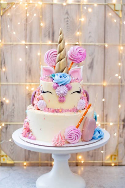 Two layered birthday unicorn cake with golden fondant horn, eyelashes and cream cheese frosting on festive christmas bokeh background